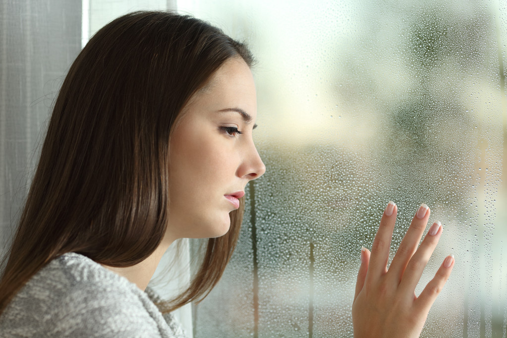 Traurige Frau blickt durch ein Fenster auf Regen - Foto, Bild