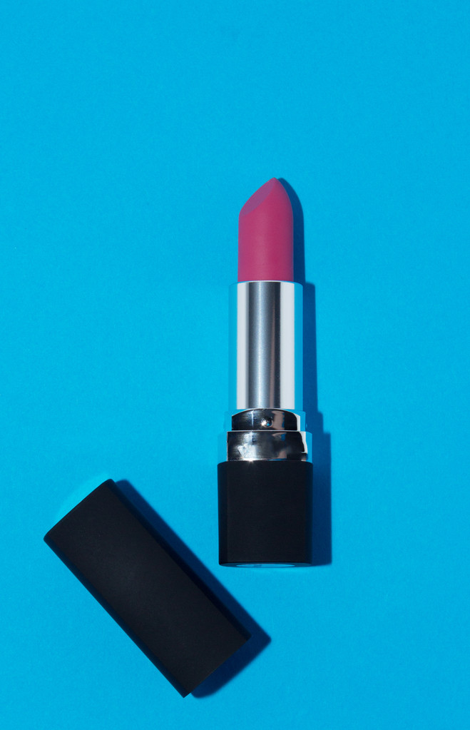 Lápiz labial rosa en tubo negro y plateado sobre fondo azul
 - Foto, Imagen