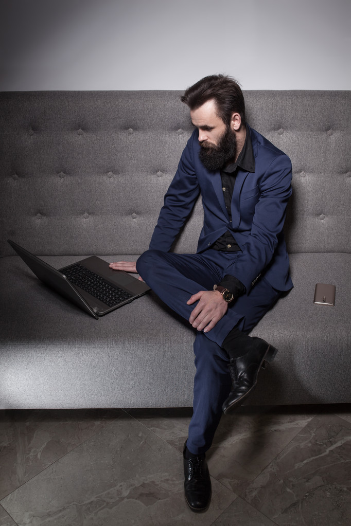 γενειοφόρος άνδρας ντυμένος με κοστούμι και με laptop περιήγηση στο internet; - Φωτογραφία, εικόνα