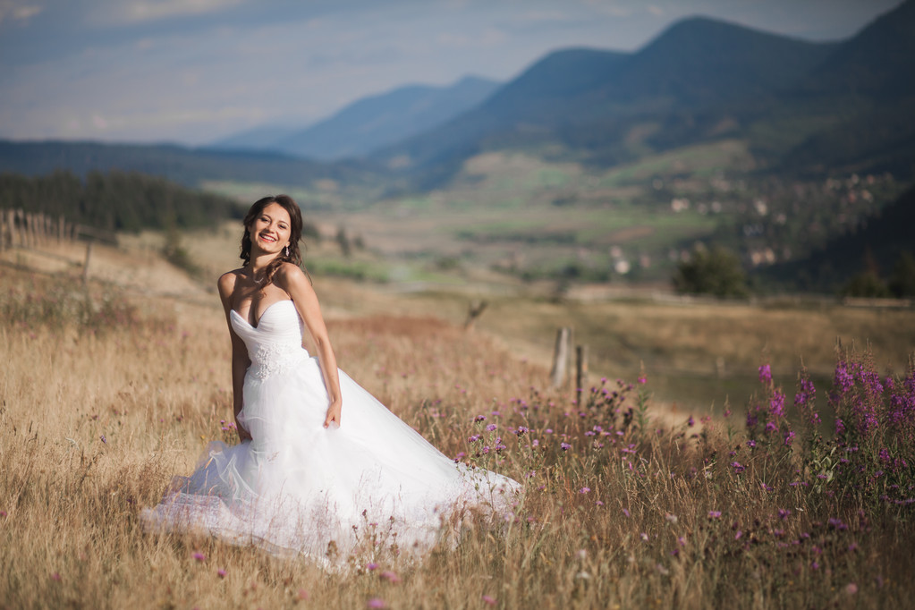 Nádherná nevěsta v elegantní šaty pózuje na slunečný letní den na pozadí hory - Fotografie, Obrázek