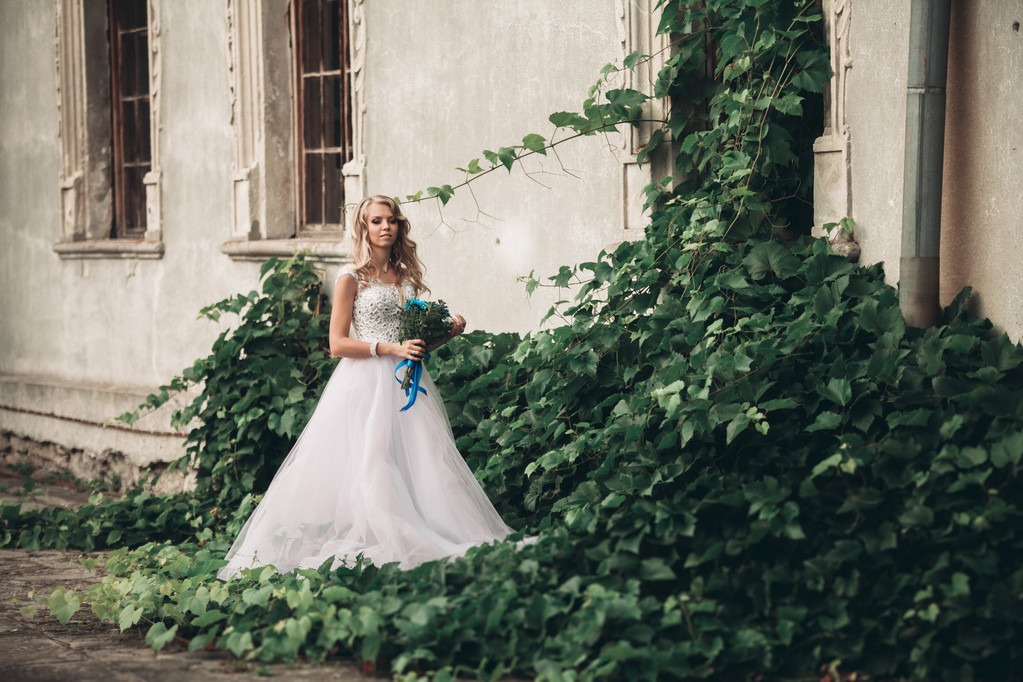 Роскошная молодая блондинка невеста с свадебным букет позы на заднем плане великолепные растения
 - Фото, изображение