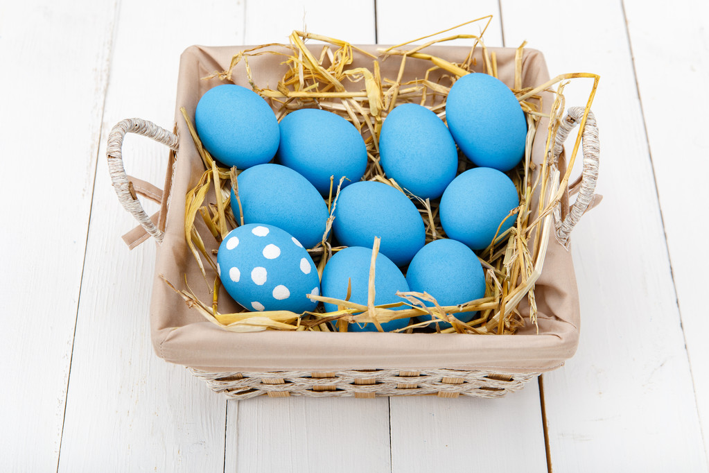 Голубые пасхальные яйца в корзине на белом деревянном столе
 - Фото, изображение