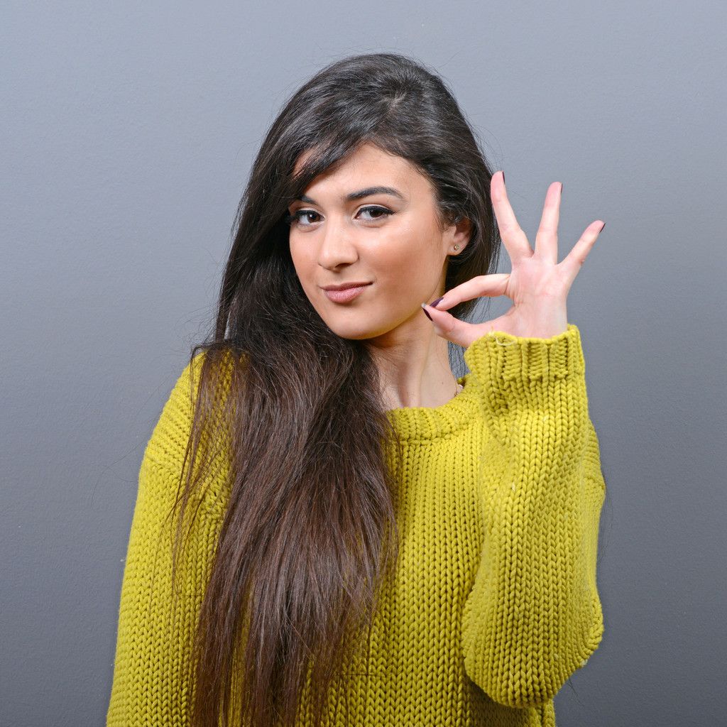 Portrait of happy woman showing ok sign against gray background - Photo, Image