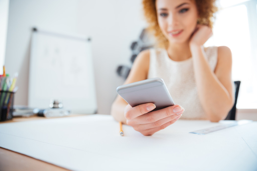 Empresária ruiva encaracolado atraente sentado e usando smartphone
  - Foto, Imagem