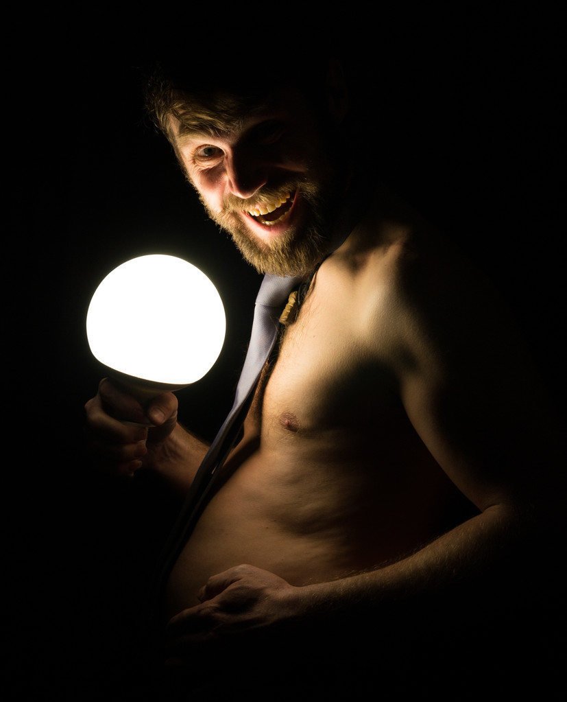 bebaarde man met een grote buik in een gelijkspel op een naakte lichaam houden een grote lamp - Foto, afbeelding