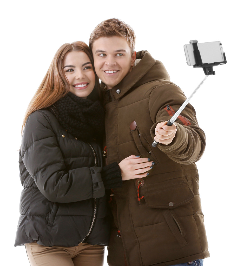 Pareja adolescente en ropa de invierno haciendo foto por su cuenta con teléfono móvil, aislado en blanco
 - Foto, Imagen