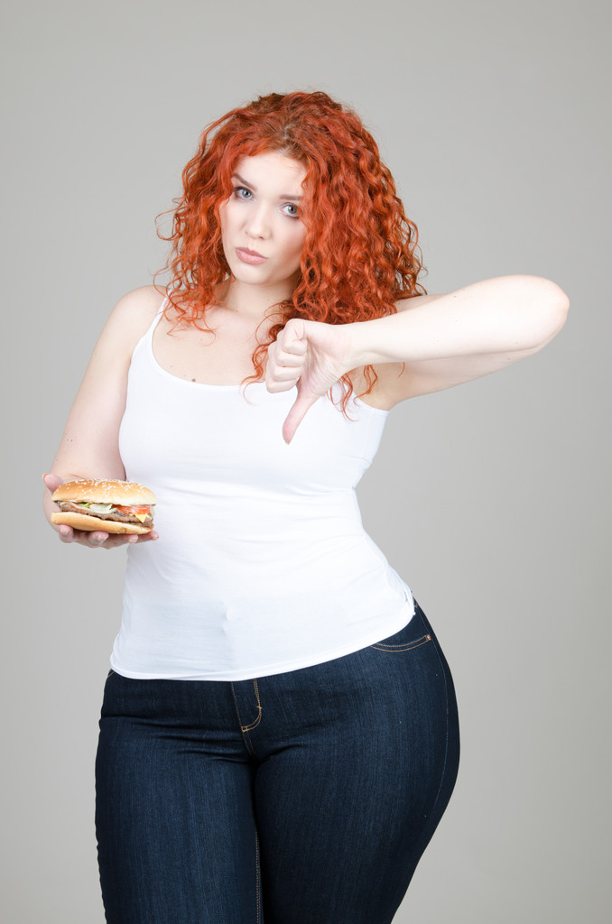 hermosa chica gorda con el pelo rojo con hamburguesa en la mano sobre fondo gris
 - Foto, Imagen