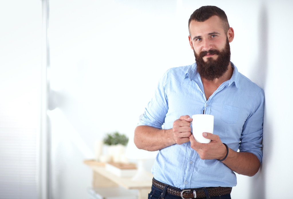 mladý muž stál u zdi a drží šálek kávy - Fotografie, Obrázek