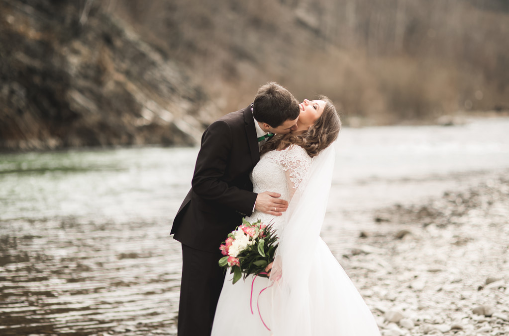 Couple de mariage heureux, mariée et marié posant rivière soignée sur fond de montagnes
 - Photo, image