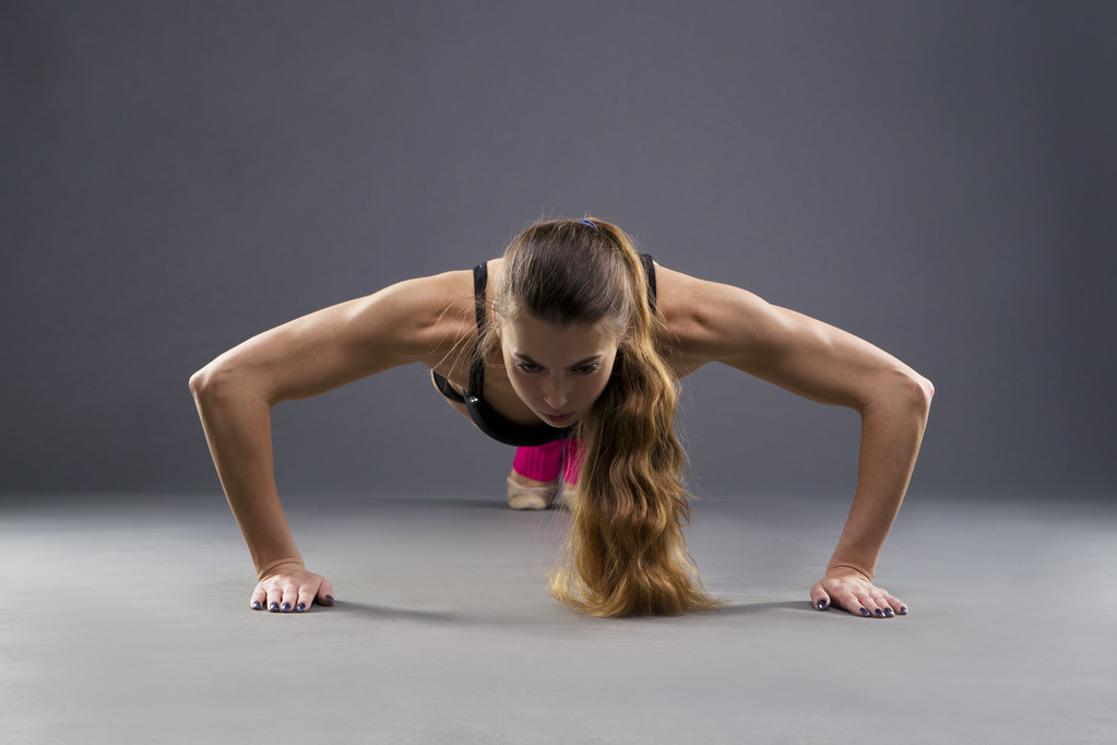 Beautiful young muscular woman doing push ups in studio - Photo, Image