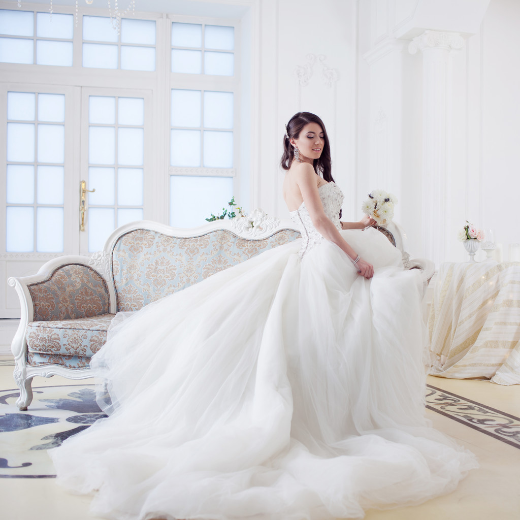 ソファーに座って壮大なドレスを着た美しい少女花嫁。豪華な光のインテリア - 写真・画像