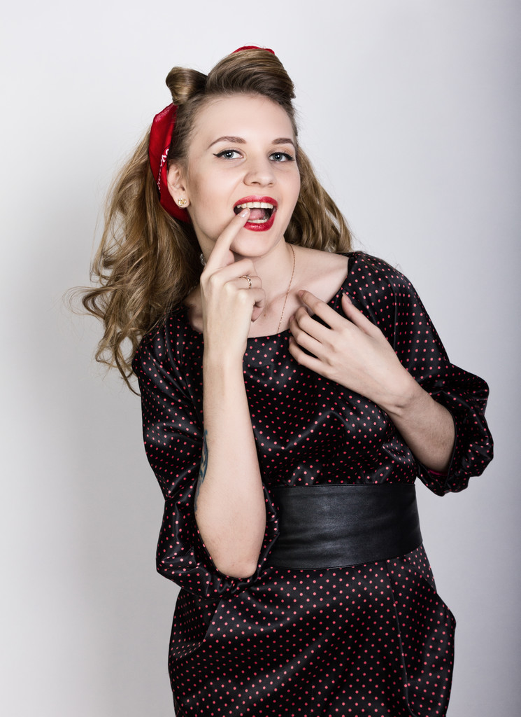jovem loira sexy com cabelos longos encaracolados em um vestido preto polka-dot, coloque seu dedo indicador em seus lábios vermelhos
 - Foto, Imagem