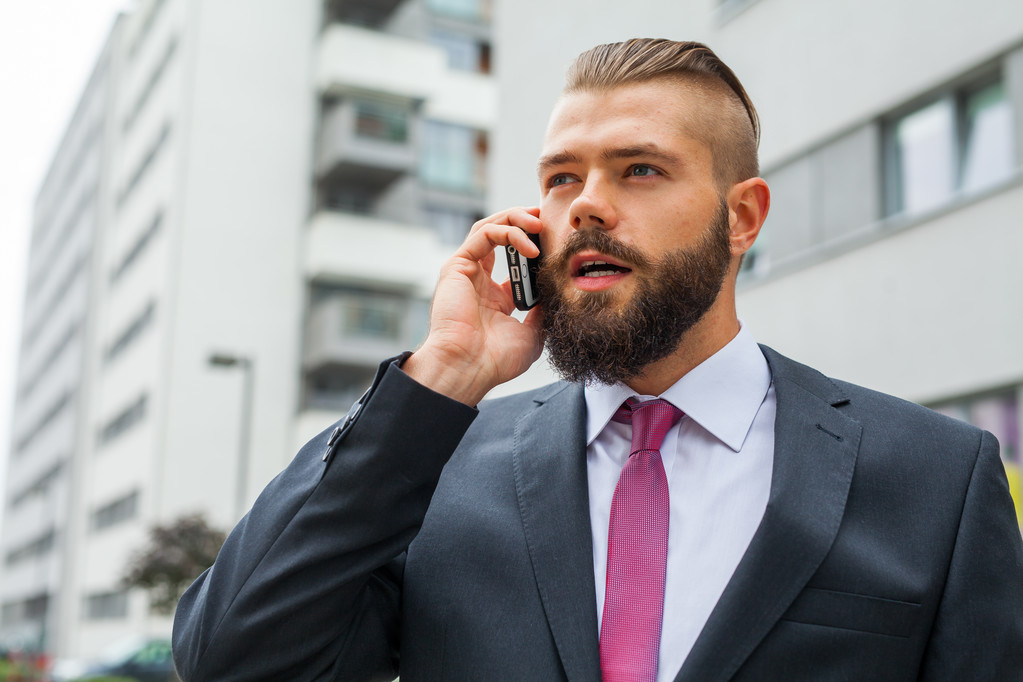 Fiatal szakállas üzletember mobiltelefon használata az irodán kívül. - Fotó, kép