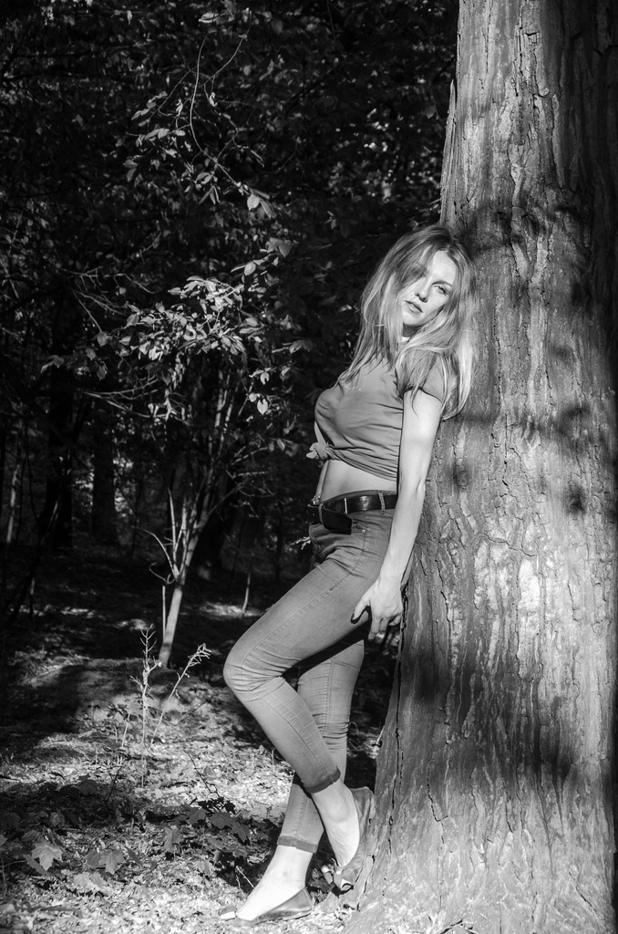 Jonge mooie sexy meisje blond model met lang blond haar in jeans en jas poseren in het bos tussen de bomen en vegetatie - Foto, afbeelding
