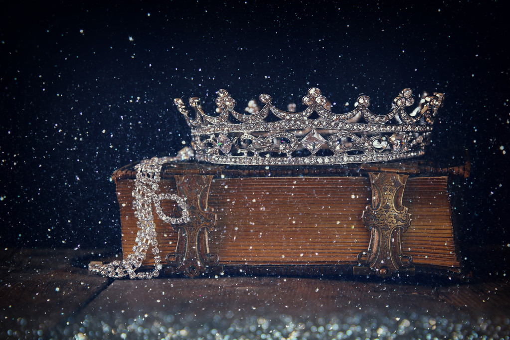 low key image of decorative crown on old book. vintage filtered  - Photo, Image