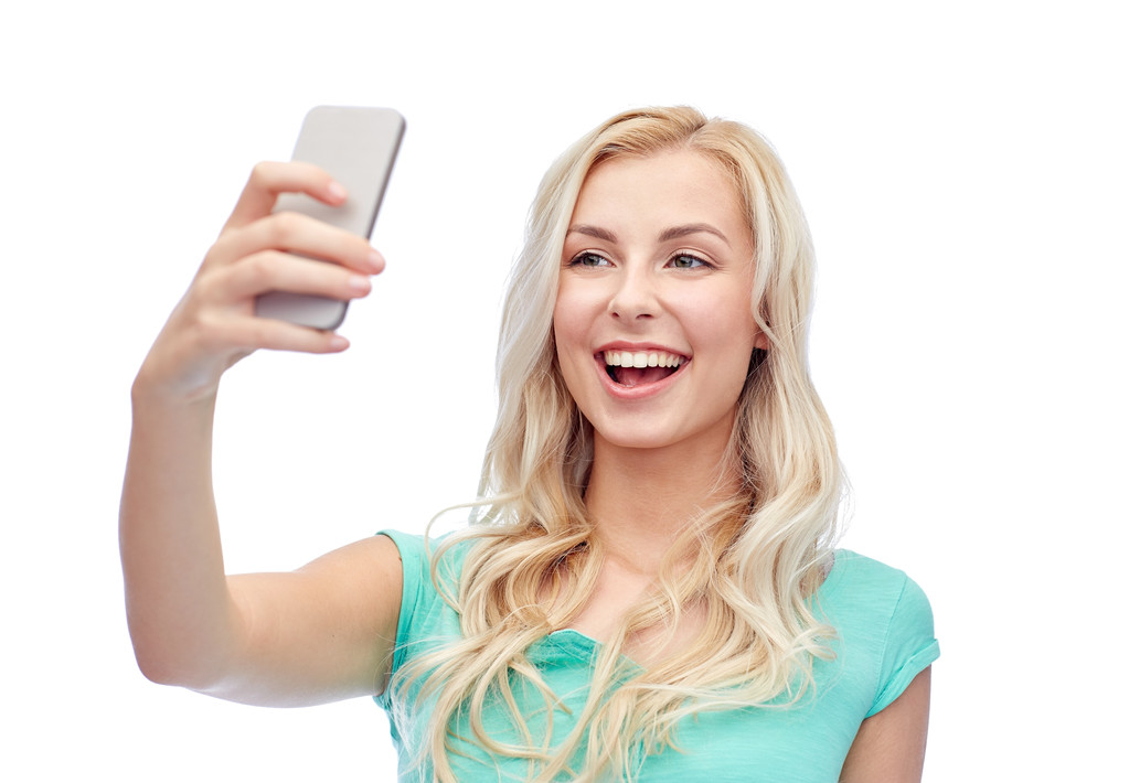 Улыбающаяся молодая женщина делает селфи со смартфоном
 - Фото, изображение