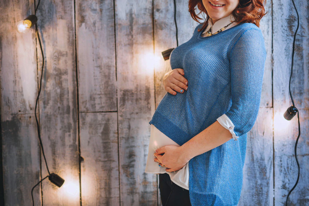 Νεαρή γυναίκα έγκυος σε μπλε στολή. Κόκκινα μαλλιά. Χαμογελάνε ευχαριστημένοι - Φωτογραφία, εικόνα