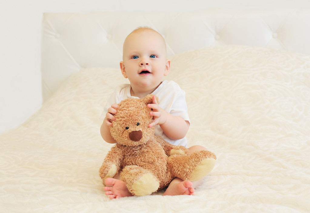 Onnellinen hymyilevä vauva leikkii nallekarhun kanssa sängyssä kotona
 - Valokuva, kuva