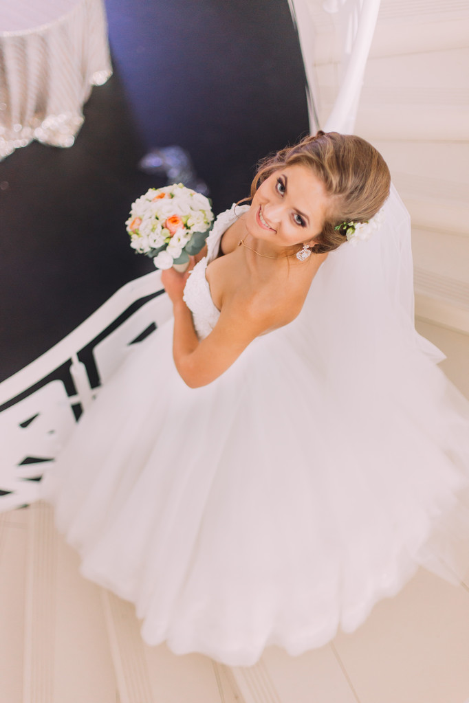 Mooie charmante bruid in een luxe jurk met boeket op zoek naar boven, bovenaanzicht - Foto, afbeelding