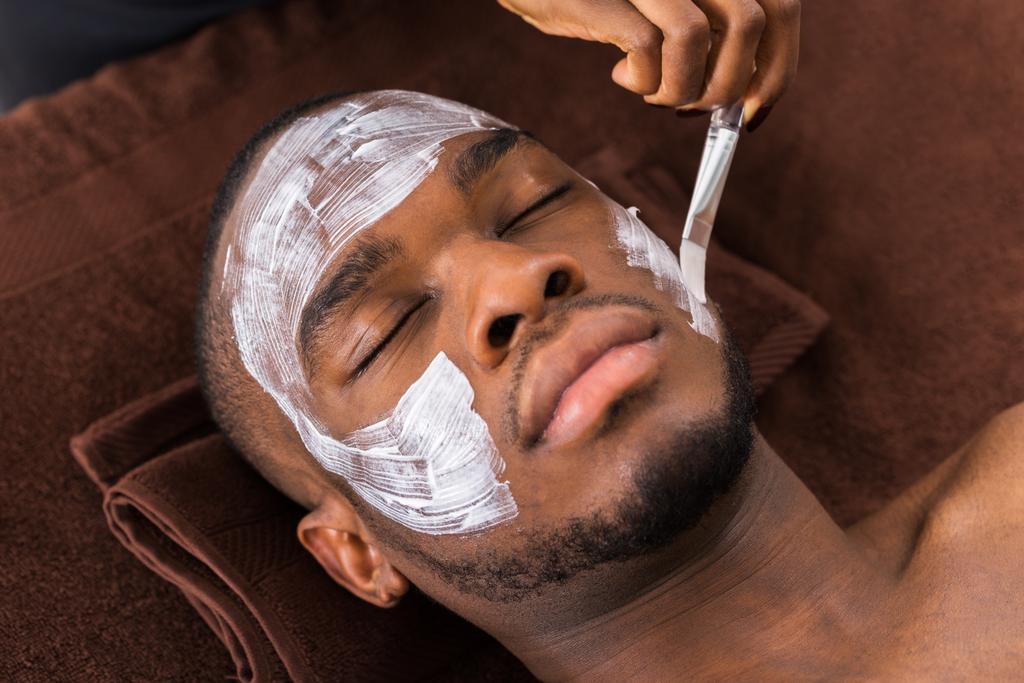 Terapeuta aplicando mascarilla facial al hombre
 - Foto, imagen