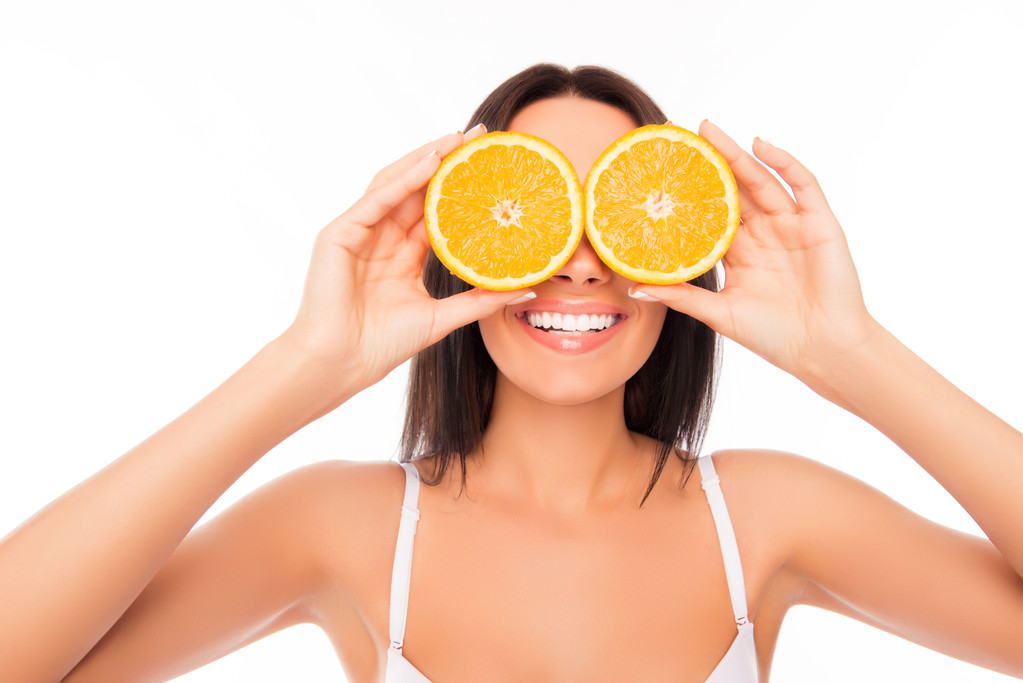 Primer plano retrato de la mujer divertida sosteniendo naranja cerca de los ojos
 - Foto, imagen