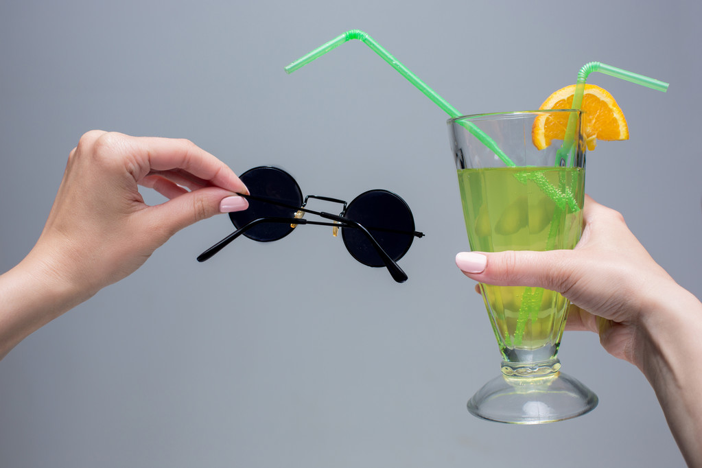 Les mains féminines avec cocktail et lunettes de soleil sur fond gris
 - Photo, image