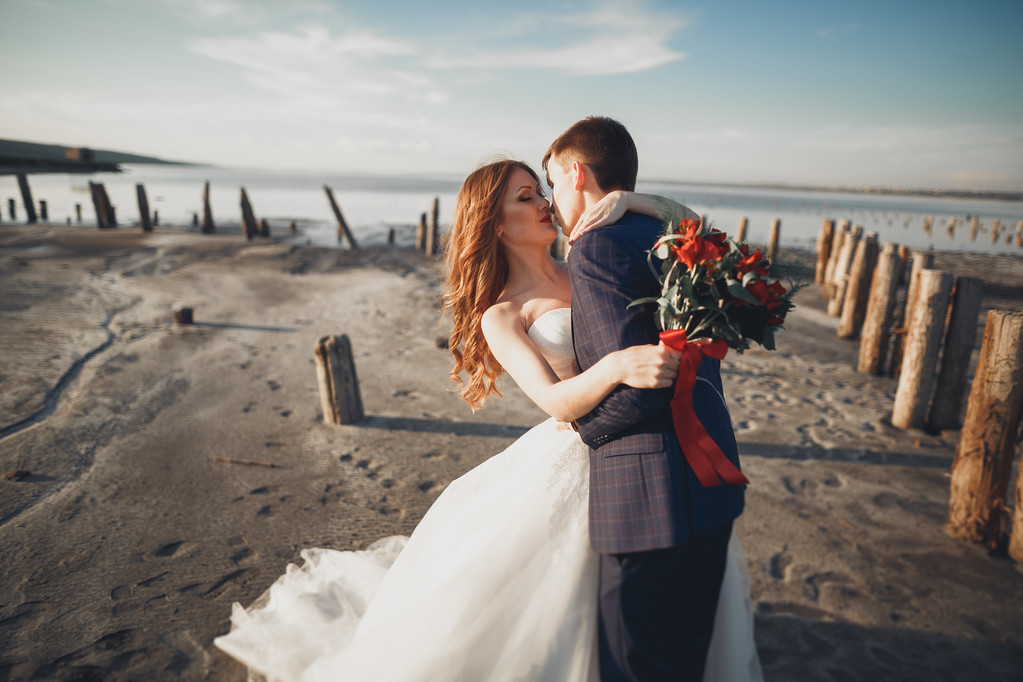 Elegáns elegáns boldog esküvő pár, menyasszony, gyönyörű vőlegény a háttérben a tenger és az ég - Fotó, kép