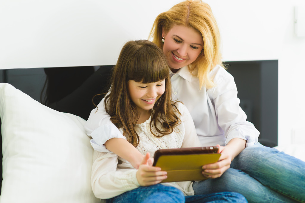 happy family. Mother and daughter sitting on the bed with a tablet - Photo, Image