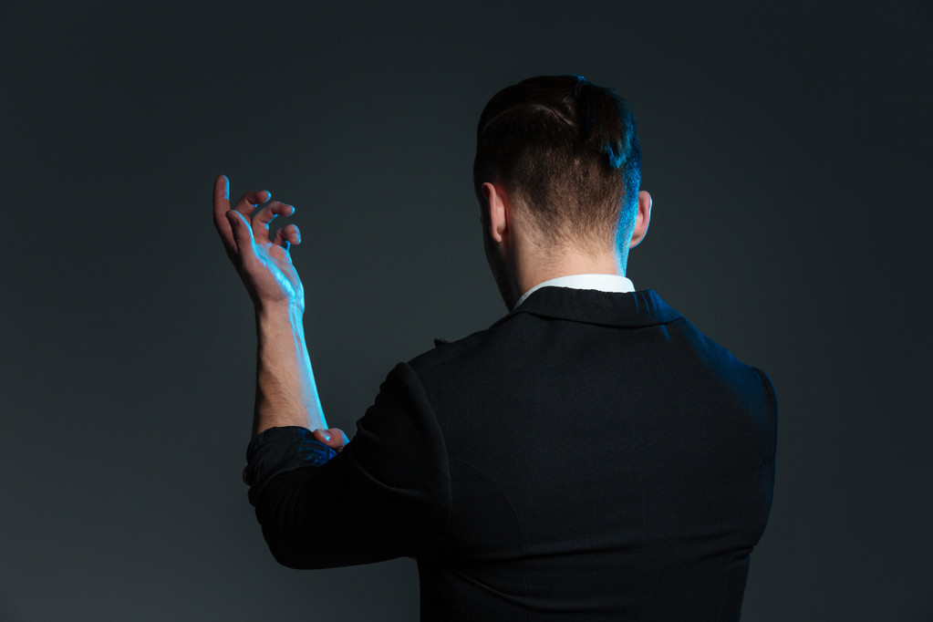 Achteraanzicht van jonge man goochelaar staande met verhoogde hand - Foto, afbeelding