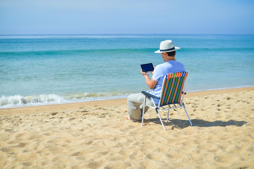 Homem usando tablet relaxante na praia do oceano, céu azul ao ar livre fundo
 - Foto, Imagem