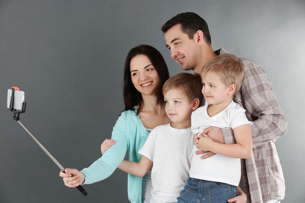 Família feliz fazendo selfie com vara de selfie no fundo cinza
 - Foto, Imagem