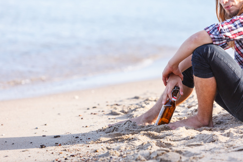 Hombre deprimido con botella de vino sentado en la playa al aire libre
 - Foto, Imagen