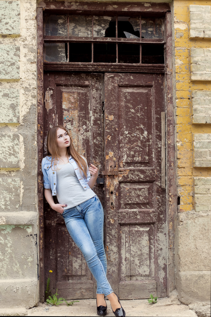hermosa joven dulce chica con el pelo rojo en jeans de pie cerca de la puerta de la ciudad vieja
 - Foto, Imagen