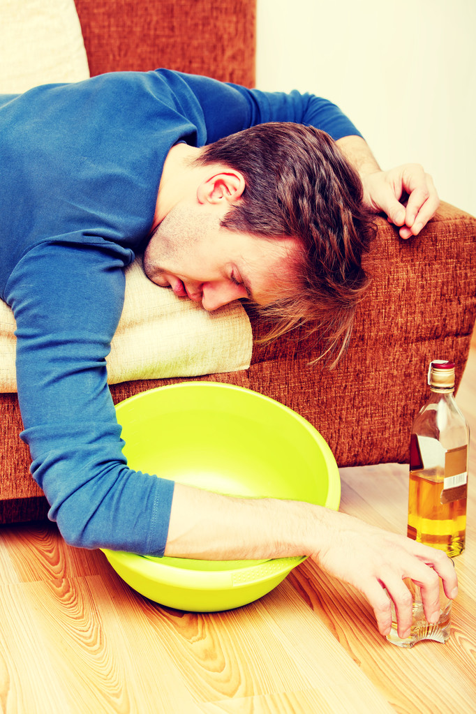 Пьяный мужчина спит на диване со взбитыми бутылками и миской - Фото, изображение