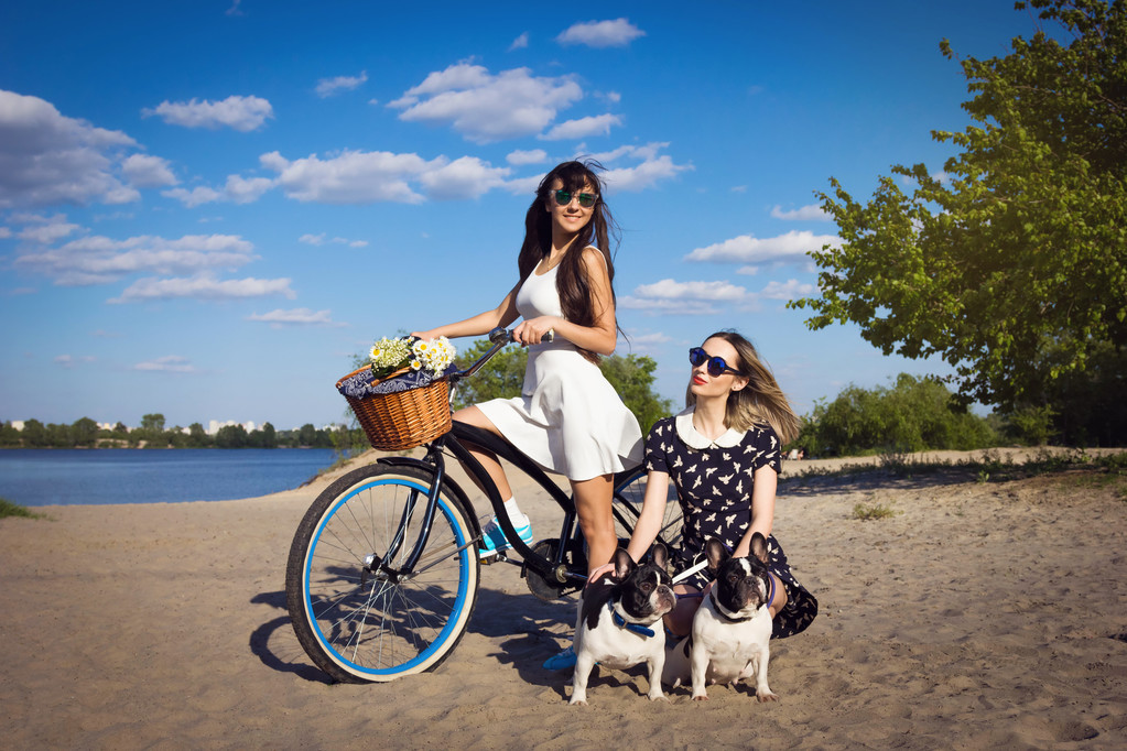 Due belle ragazze sulla spiaggia con bicicletta e bulldog francesi
 - Foto, immagini