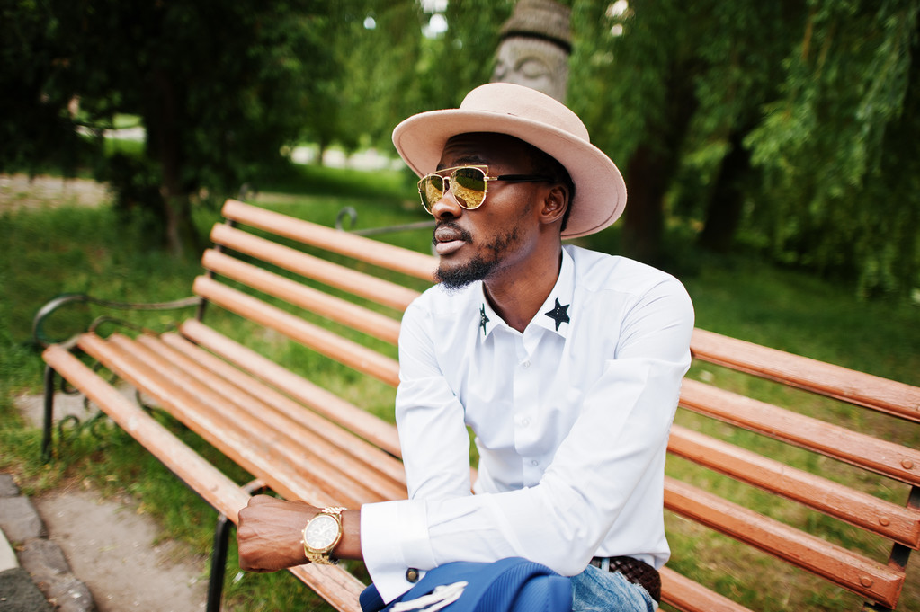 Rijke zwarte man zittend op de Bank bij Gouden zonnebril en hoed  - Foto, afbeelding