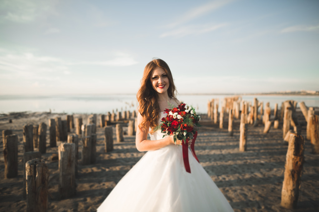 Mooie jonge bruid met bruids boeket poseren op de achtergrond-zee - Foto, afbeelding