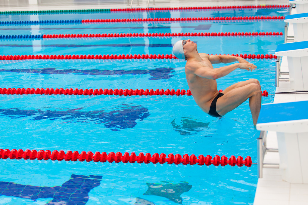Jovem nadador muscular pulando do bloco inicial em uma piscina
 - Foto, Imagem