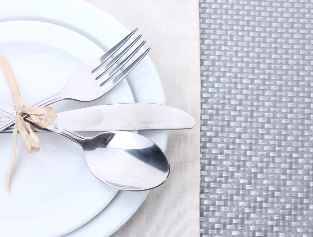 Piatti bianchi vuoti con forchetta, cucchiaio e coltello legati con un nastro su una tovaglia grigia
 - Foto, immagini