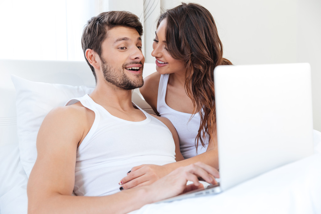 χαμογελώντας νεαρό ζευγάρι χρησιμοποιώντας φορητό υπολογιστή στο κρεβάτι - Φωτογραφία, εικόνα