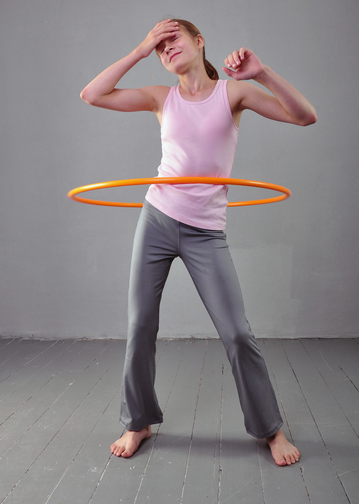 Sportliches Teenager-Mädchen macht Übungen mit Hula-Hoop-Reifen, um Muskeln auf grauem Hintergrund zu entwickeln. Spaß beim Spielen haben. Sport gesunder Lebensstil Konzept. Sportliche Kindheit. Jugendliche üben mit Werkzeug - Foto, Bild