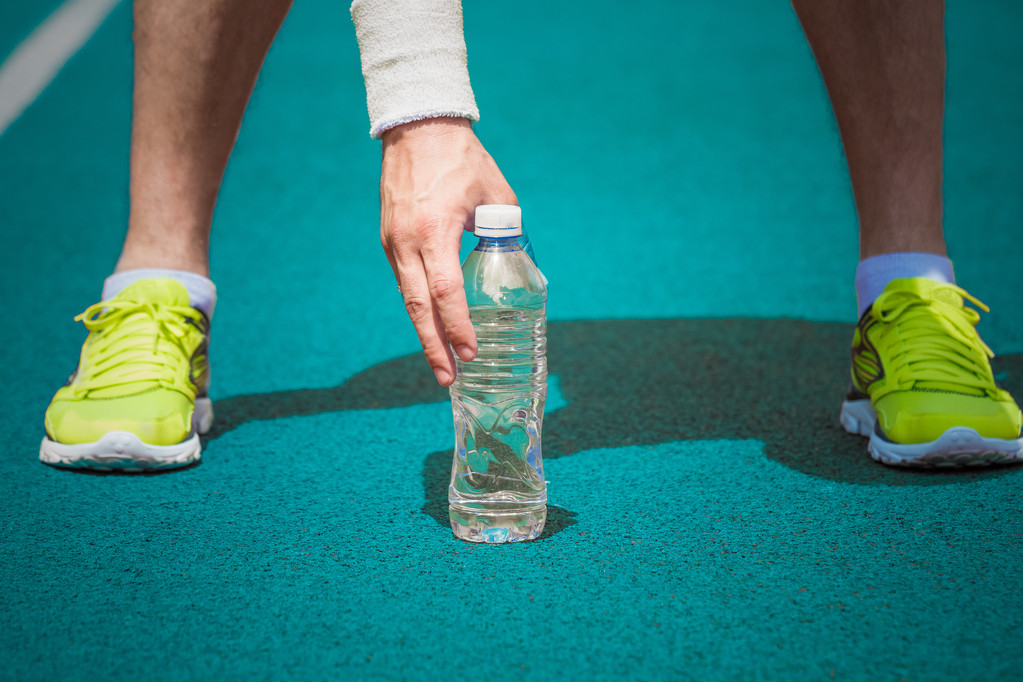 Detailní záběr mužské běžec drží plastová láhev vody na běžecké dráze - Fotografie, Obrázek