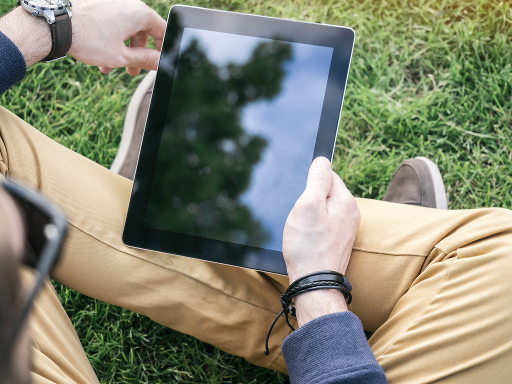 Les mains de l'homme à l'aide d'une tablette numérique Mockup avec écran blanc vierge assis sur l'herbe dans le parc
 - Photo, image
