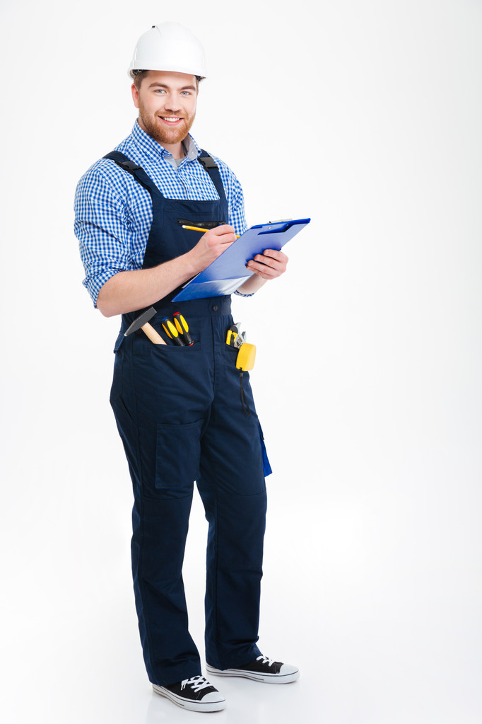 Cheerful attractive young builder standing and writing on clipboard - Photo, Image