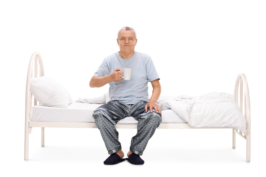 Vanhempi mies istuu sängyllä ja juo kahvia
  - Valokuva, kuva