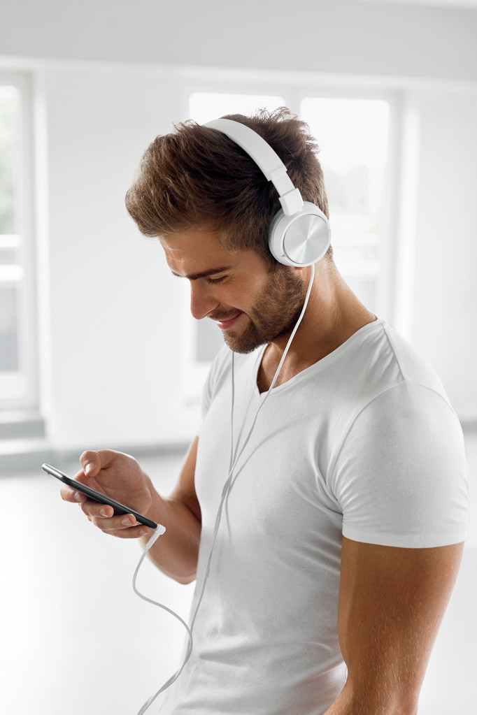 Homme écoutant de la musique dans les écouteurs utilisant un téléphone portable à l'intérieur
 - Photo, image