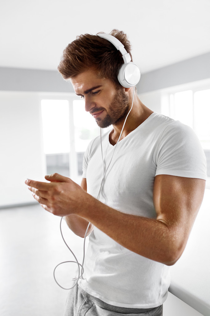 Homem ouvindo música em fones de ouvido usando telefone celular dentro de casa
 - Foto, Imagem