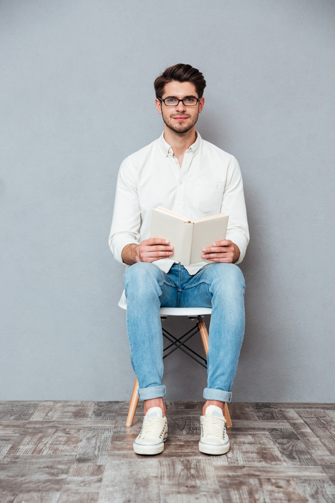 Beau jeune homme dans des lunettes assis et lisant un livre
 - Photo, image