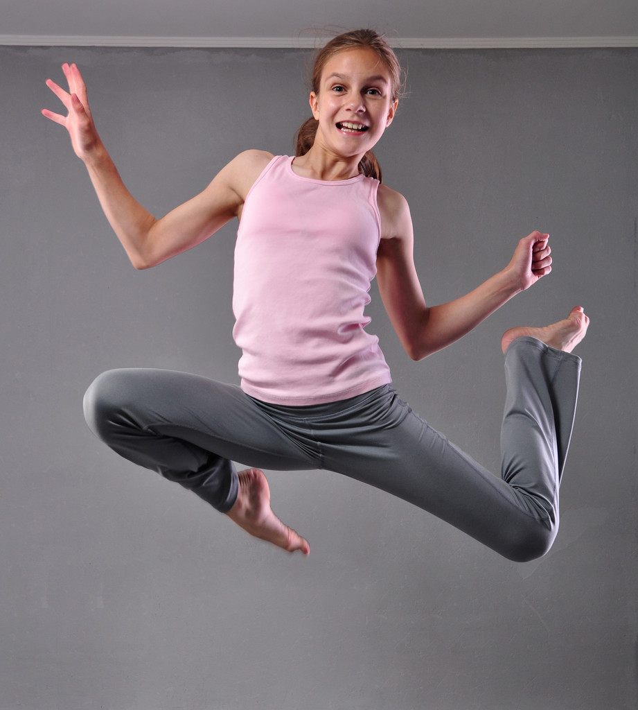 Felice sorridente ragazza ballerina adolescente saltando saltando e ballando su sfondo grigio. Esercizio per bambini. Sport sano concetto di stile di vita. Infanzia sportiva. - Foto, immagini