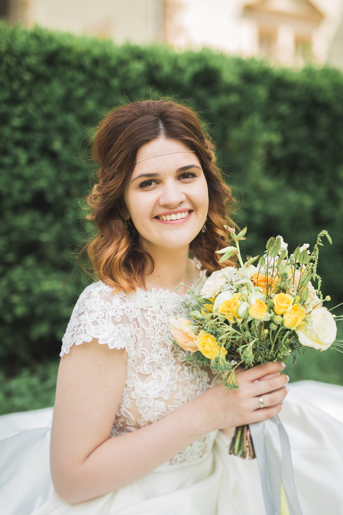 Bella sposa seduta a terra con un bouquet sorridente alla macchina fotografica
 - Foto, immagini